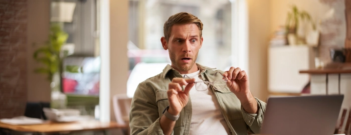 portrait-d-un-homme-dans-un-cafe-qui-enleve-ses-lunettes-semble-choque-et-preoccupe-par-l-ecran-de-son-ordinateur-portable-lisant-des-nouvelles-bouleversantes
