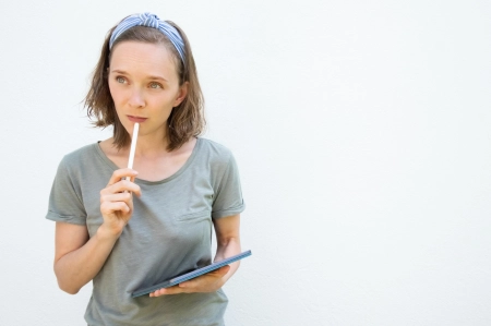 UNE FEMME TIENT UN CRYAON ET RÉFLÉCHIT SUR SON BLOC NOTE