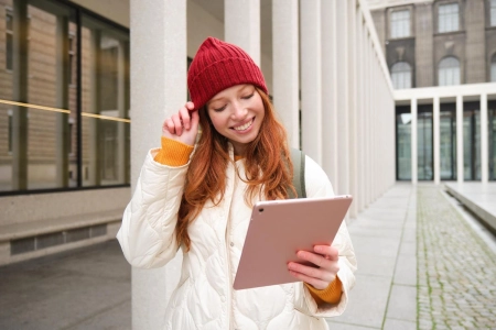 Heureuse rousse au chapeau rouge se promène dans la ville avec une tablette